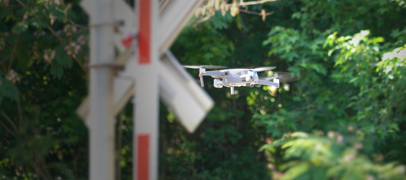 Photo of a drone hovering near a railroad crossbuck and gate, with a forest in the background.