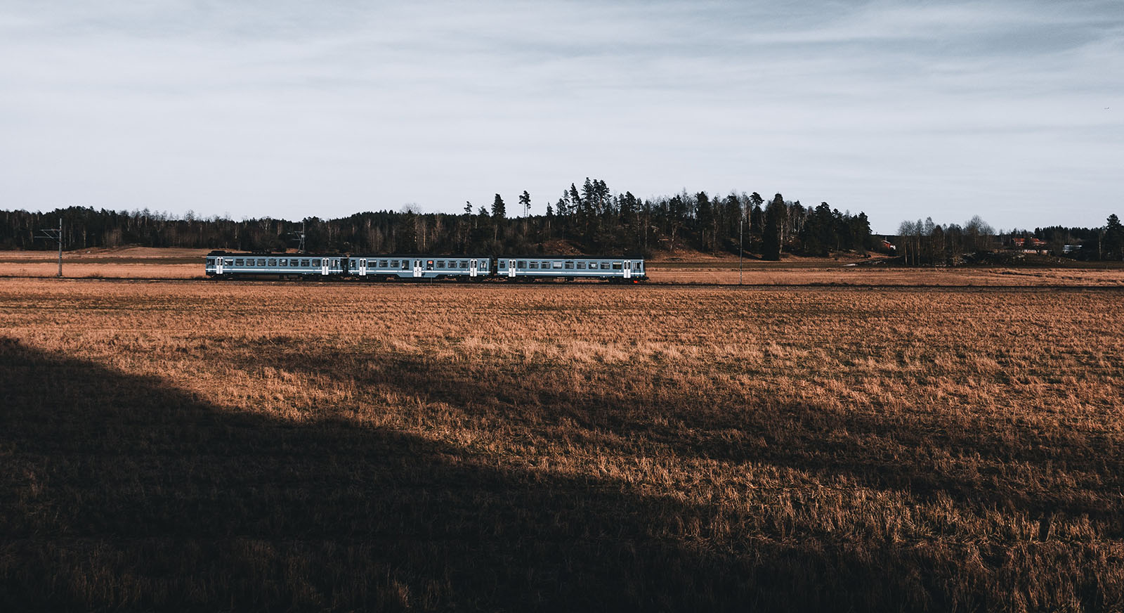 Photo of a short silver train cutting across an amber field, with a gray cloudy sky in the background