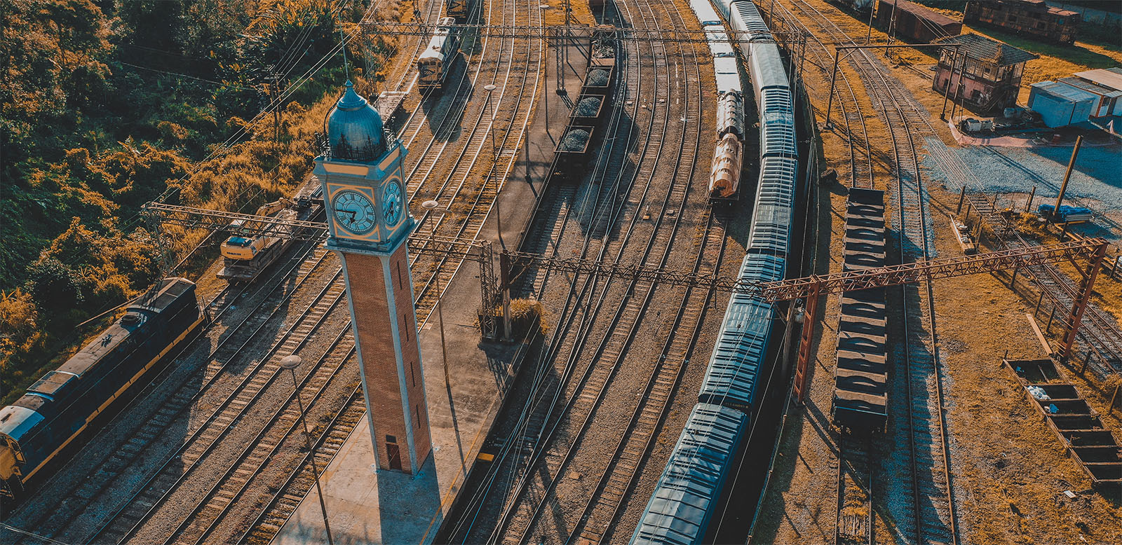 Photo of a rail yard in a tropical location, with train cars and a clock tower.