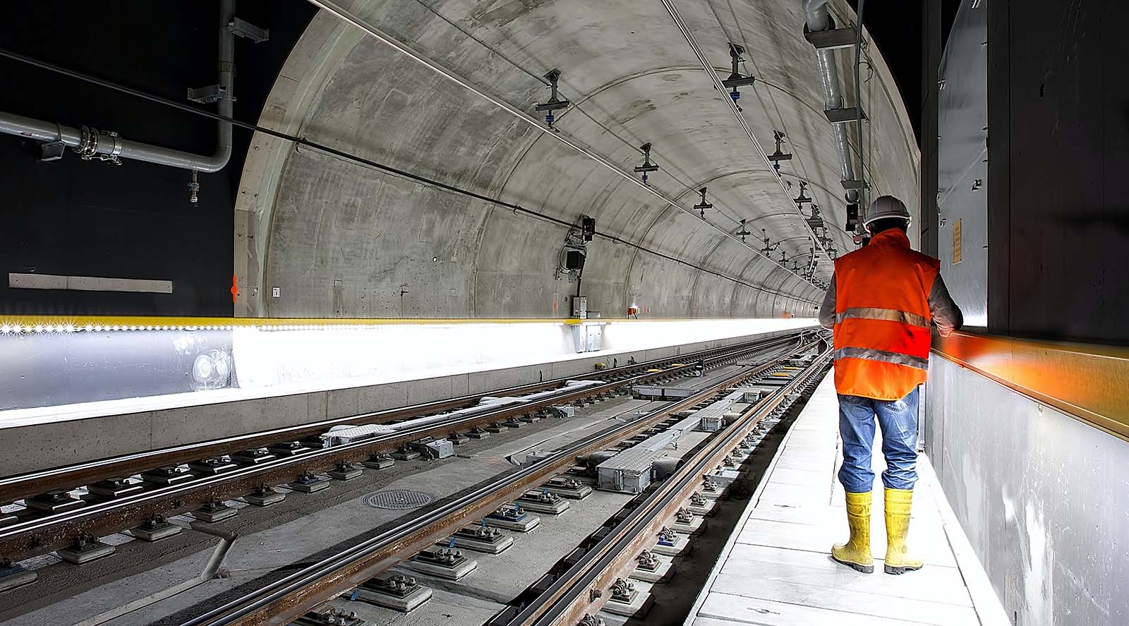 Photo of a rail inspector standing in a railway tunnel, looking down the track with their back turned to us.